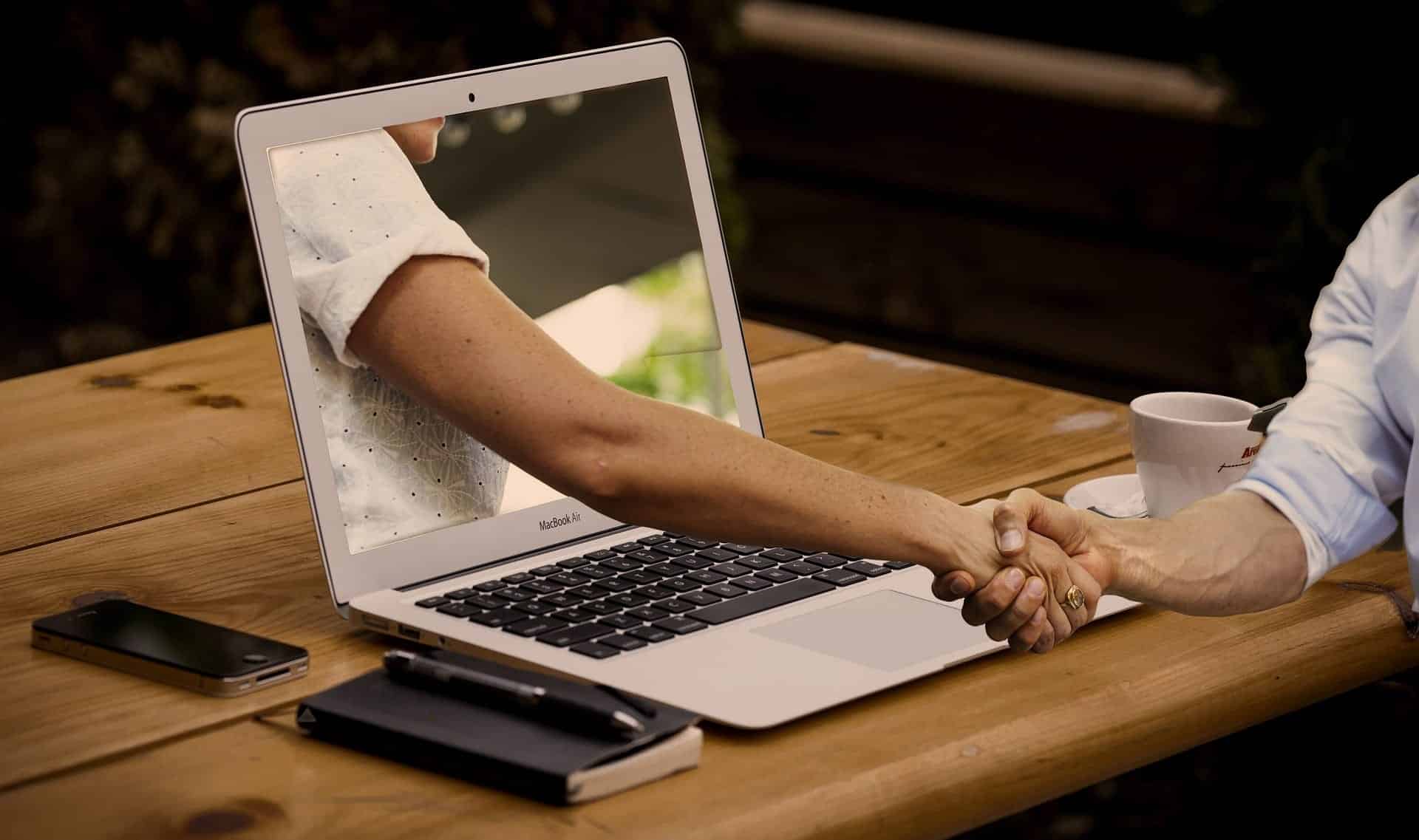 Handshake through a laptop screen representing AI-assisted collaboration in nonprofit grant reporting